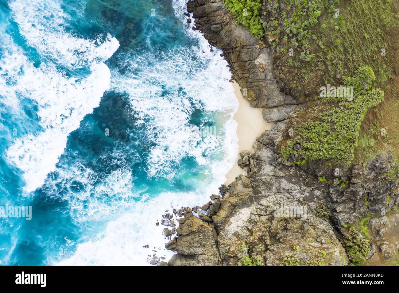 Beeindruckende Luftaufnahme von einem versteckten Strand vom türkisfarbenen Meer gebadet und von einem grünen felsigen Klippen flankiert. Insel Lombok, West Nusa Tenggara, Indonesien. Stockfoto