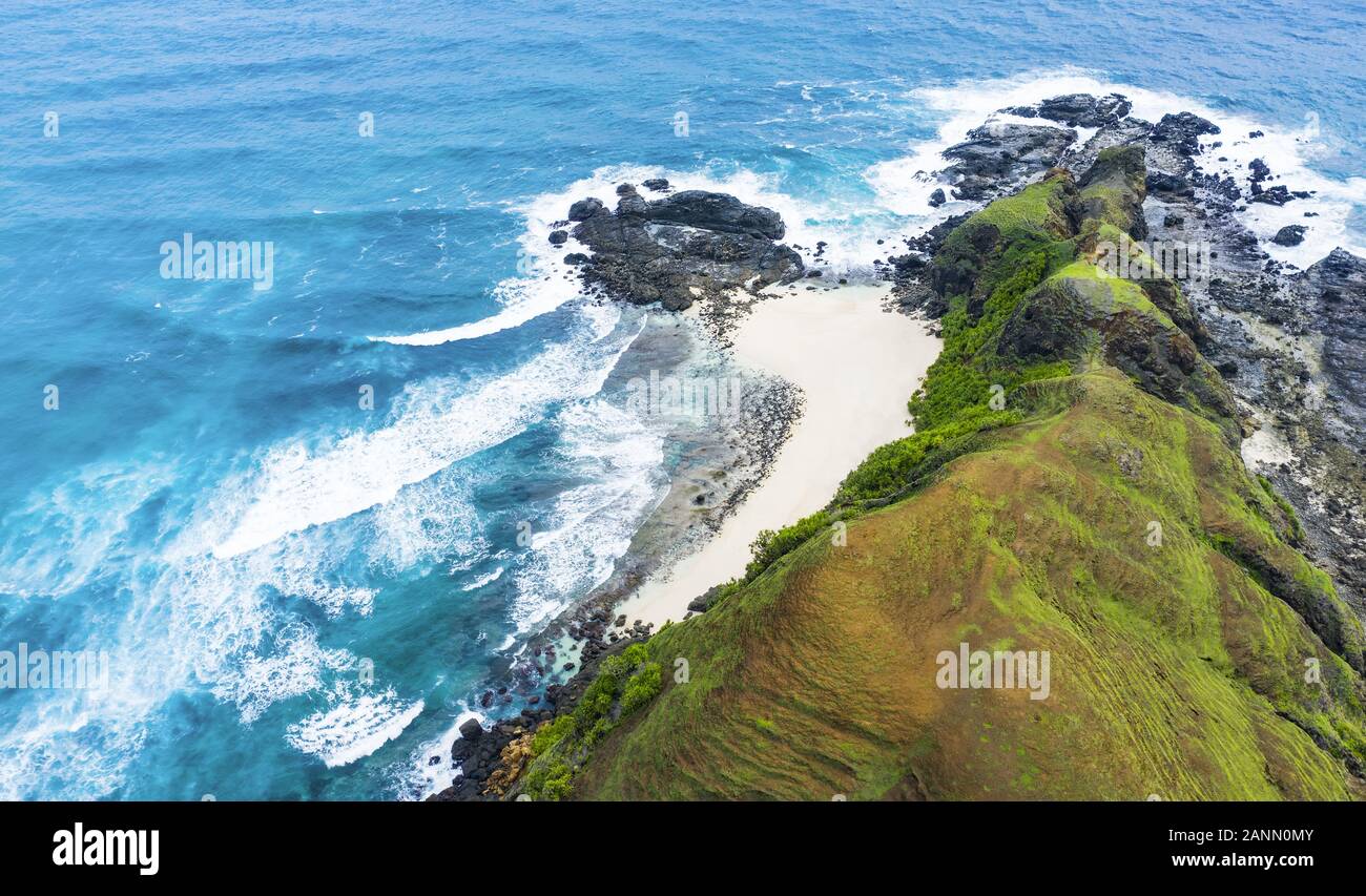 Beeindruckende Luftaufnahme von einem versteckten Strand vom türkisfarbenen Meer gebadet und von einem grünen felsigen Klippen flankiert. Insel Lombok, West Nusa Tenggara, Indonesien. Stockfoto