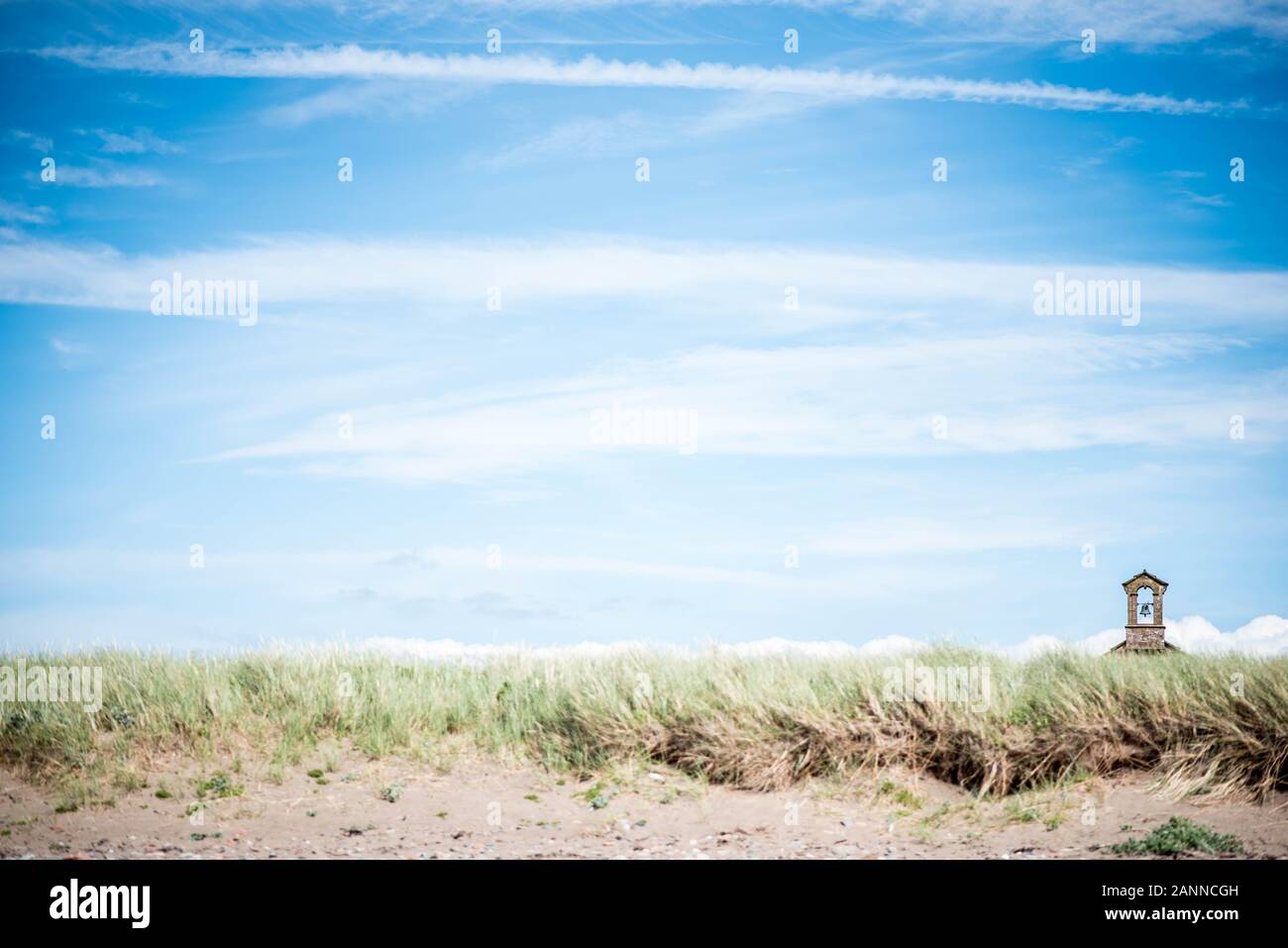 Landschaftsbild von grasbedeckten Sanddünen bei Allonby in Cumbria mit dem Kirchturm der Christuskirche am sonnigen Tag Stockfoto