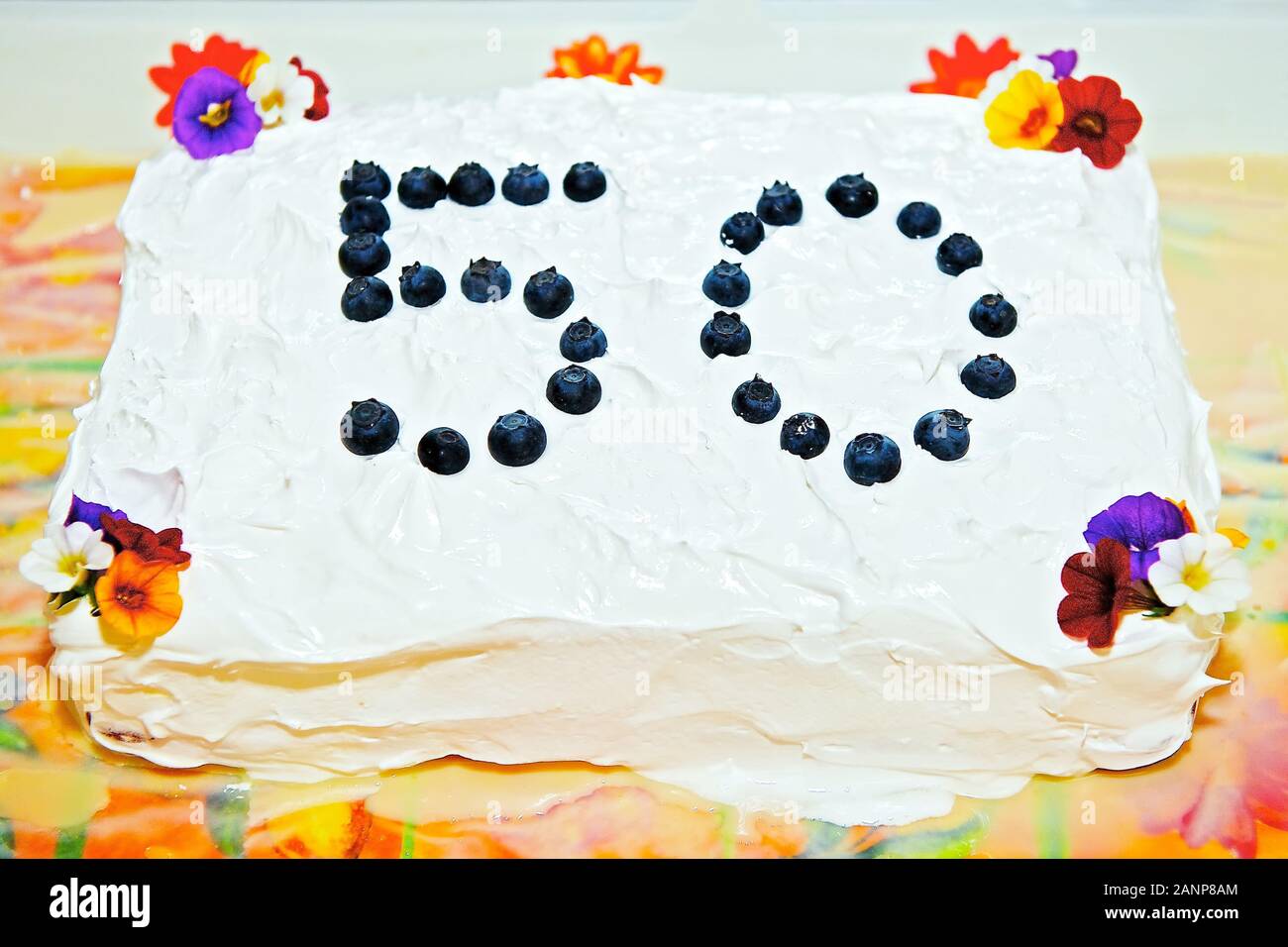 Hausgemachte Kuchen mit weißer Glasur, mit Blumen und blaubeeren eingerichtet, feiert den 50. Geburtstag Stockfoto