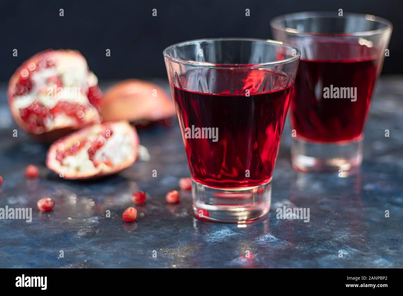 Granatapfelsaft in transparenten Gläsern. Im Hintergrund sind Teile eines großen Granatapfel. Auf einem blauen Hintergrund unter einem Stein. Trend 2020. Körner, die einen Stockfoto