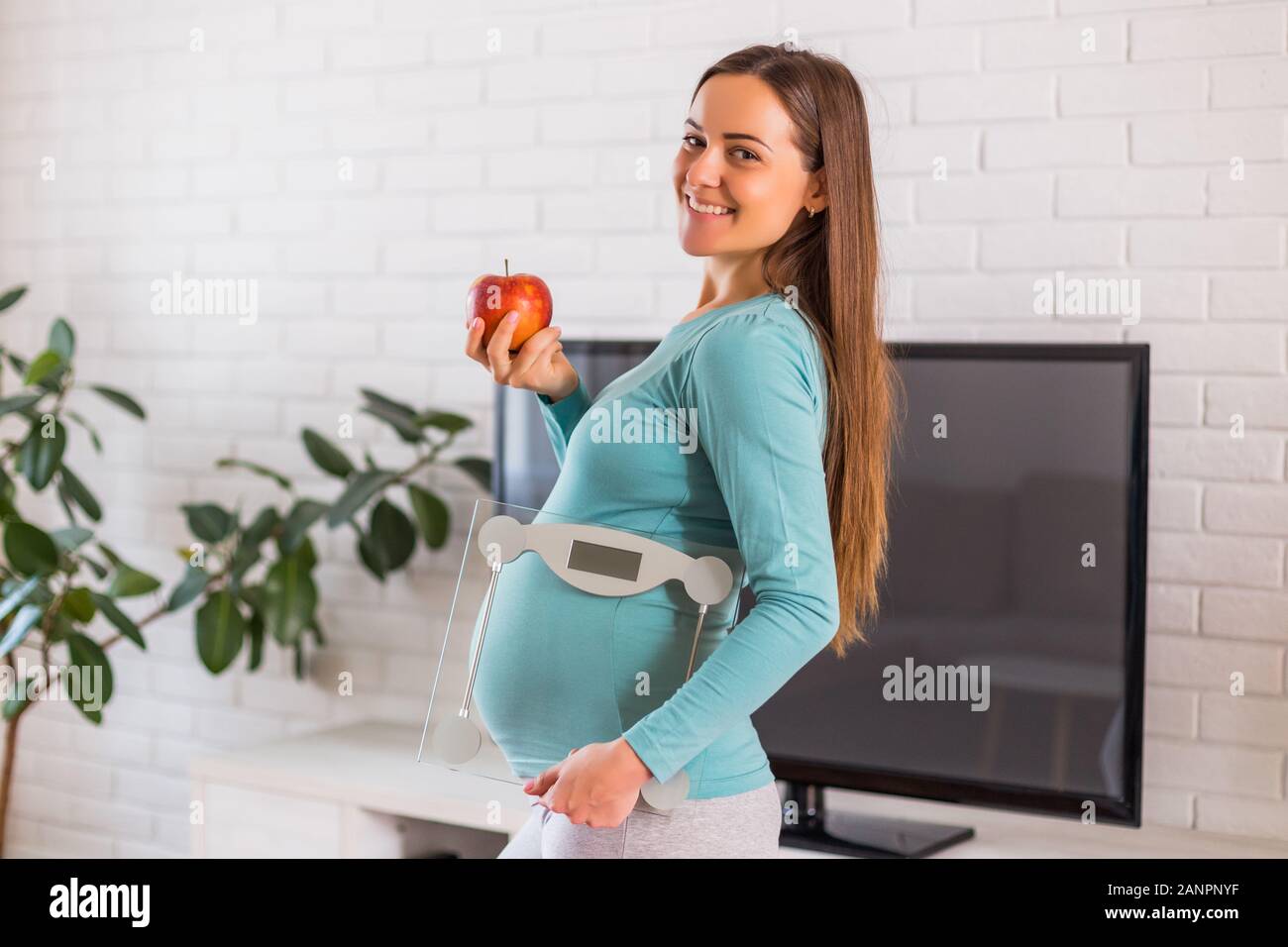 Frau mit Apfel, Maßstab und zeigen, dass Sie gesund essen und trainieren, während sie schwanger ist. Stockfoto