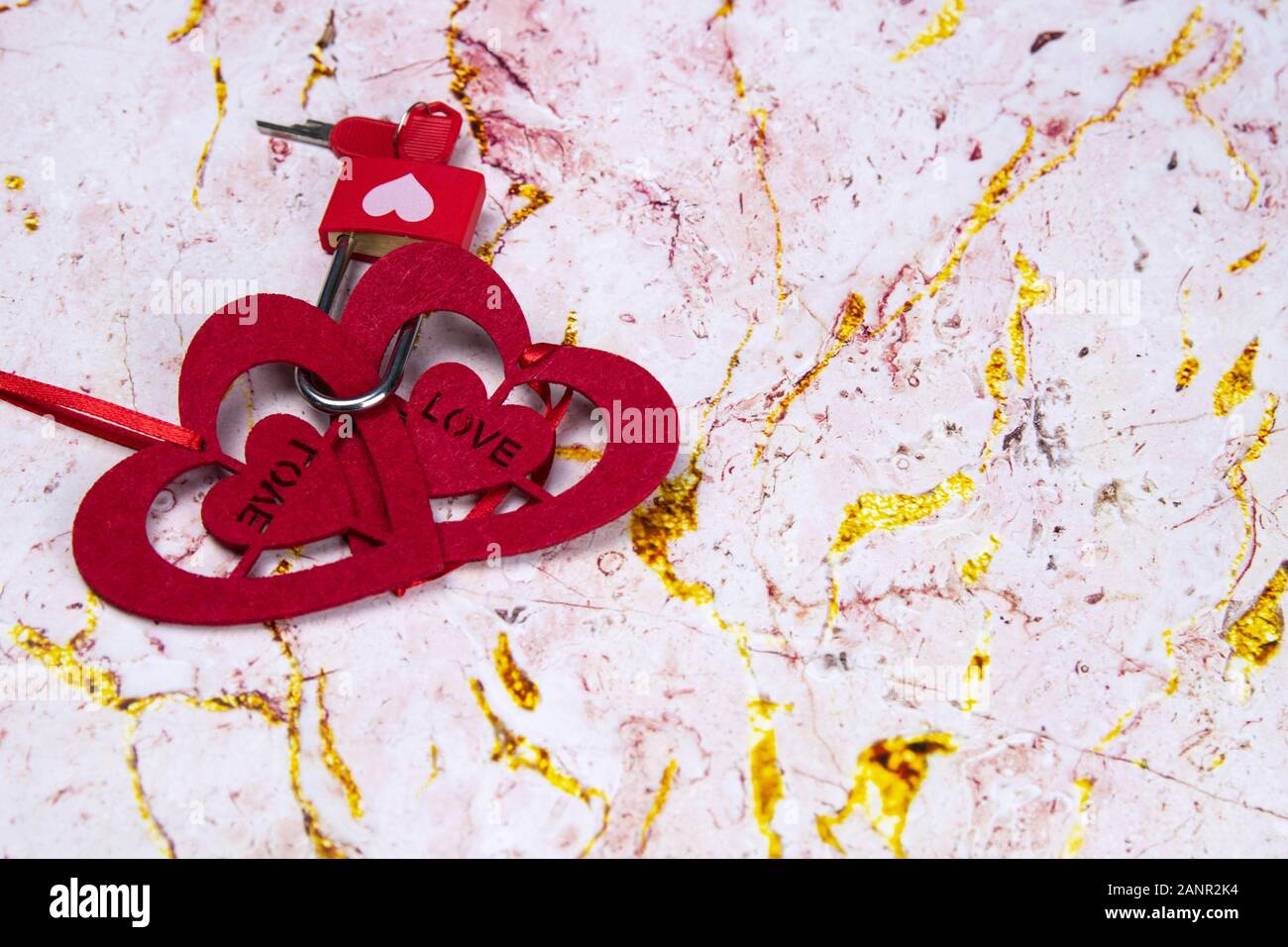 Zwei Herzen aus Filz sind durch einen Block mit einem Schlüssel auf einem Marmor rosa Hintergrund verbunden. Schlüssel zu meinem Herzen Konzept. Mit Platz kopieren Stockfoto