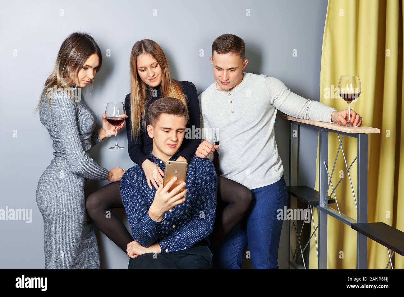 Junge Männer und Frauen sind Fotos von student Party auf dem Bildschirm eines Handys oder Smartphones. Studenten kommunizieren in einem Zimmer in einem Studentenwohnheim, watc Stockfoto