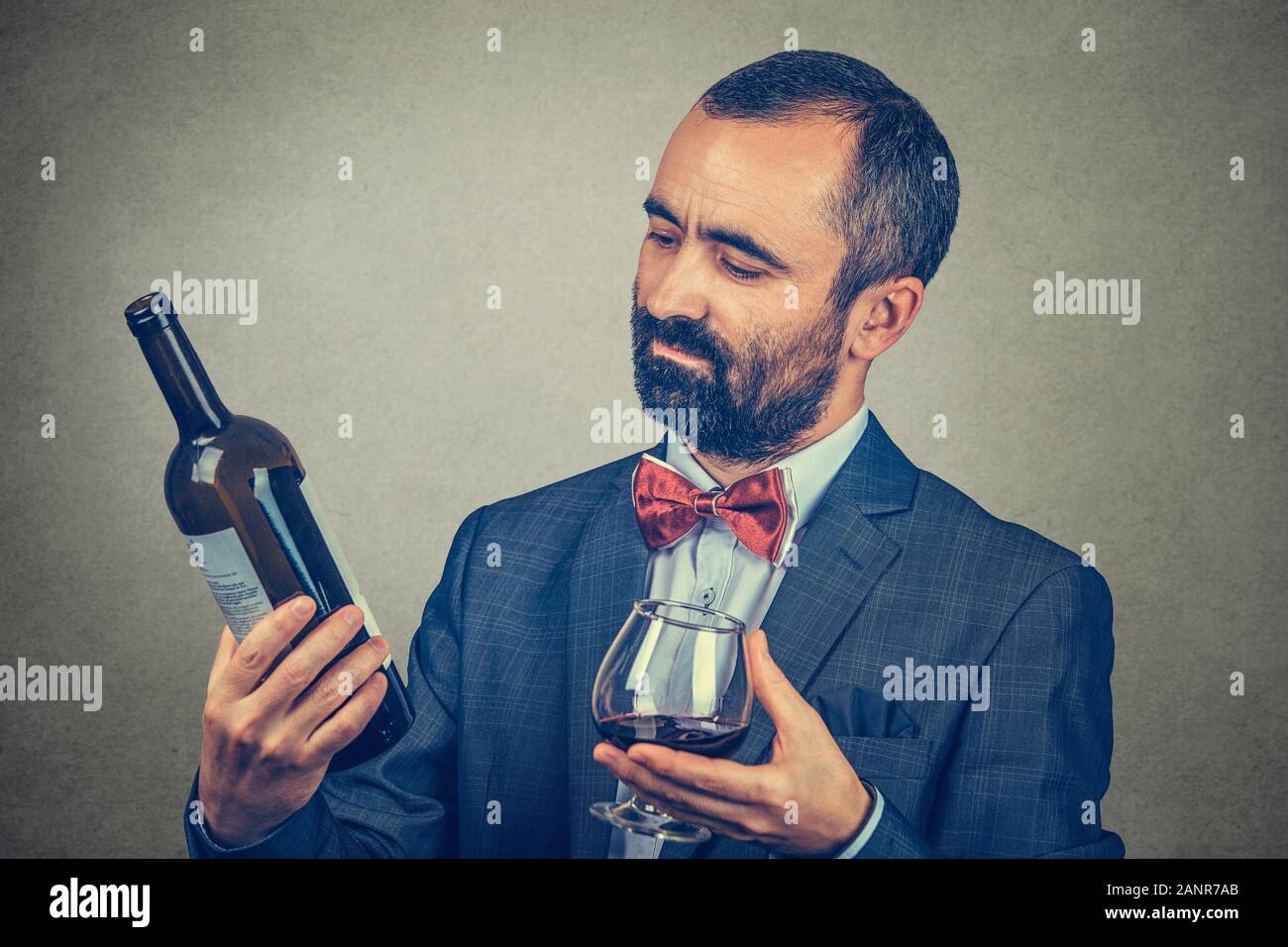 Ein Mann mit einem Glas Wein Holding, eine Flasche suchen, lesen Sie die Informationen über Sie. Gemischte Rasse bearded Modell auf grauem Hintergrund. Horizo Stockfoto