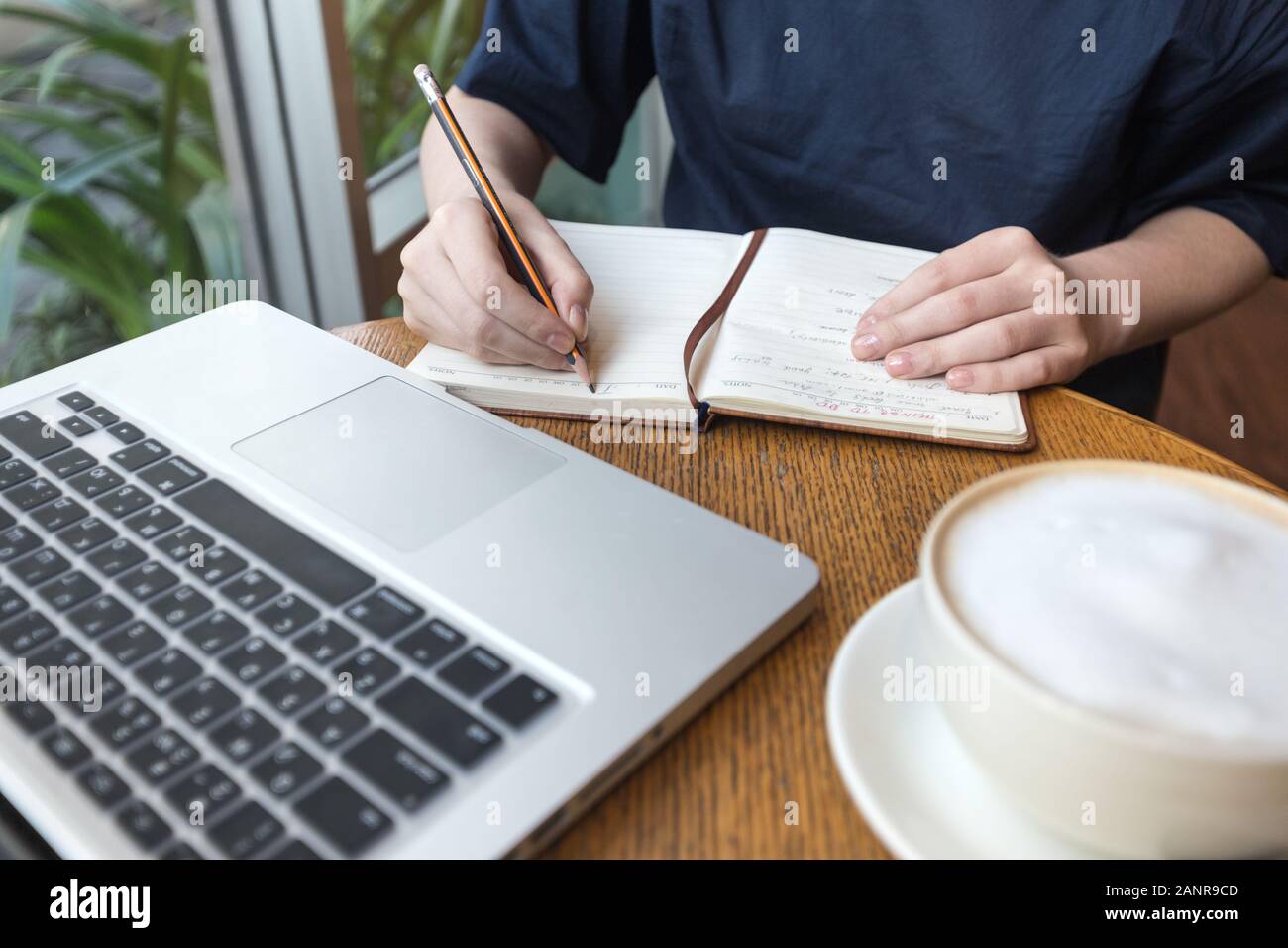 Frauenhände mit Kaffeetasse, Laptop und Notebook, die Notizen für Geschäfte auf dem Tisch machen, aus nächster Nähe Stockfoto