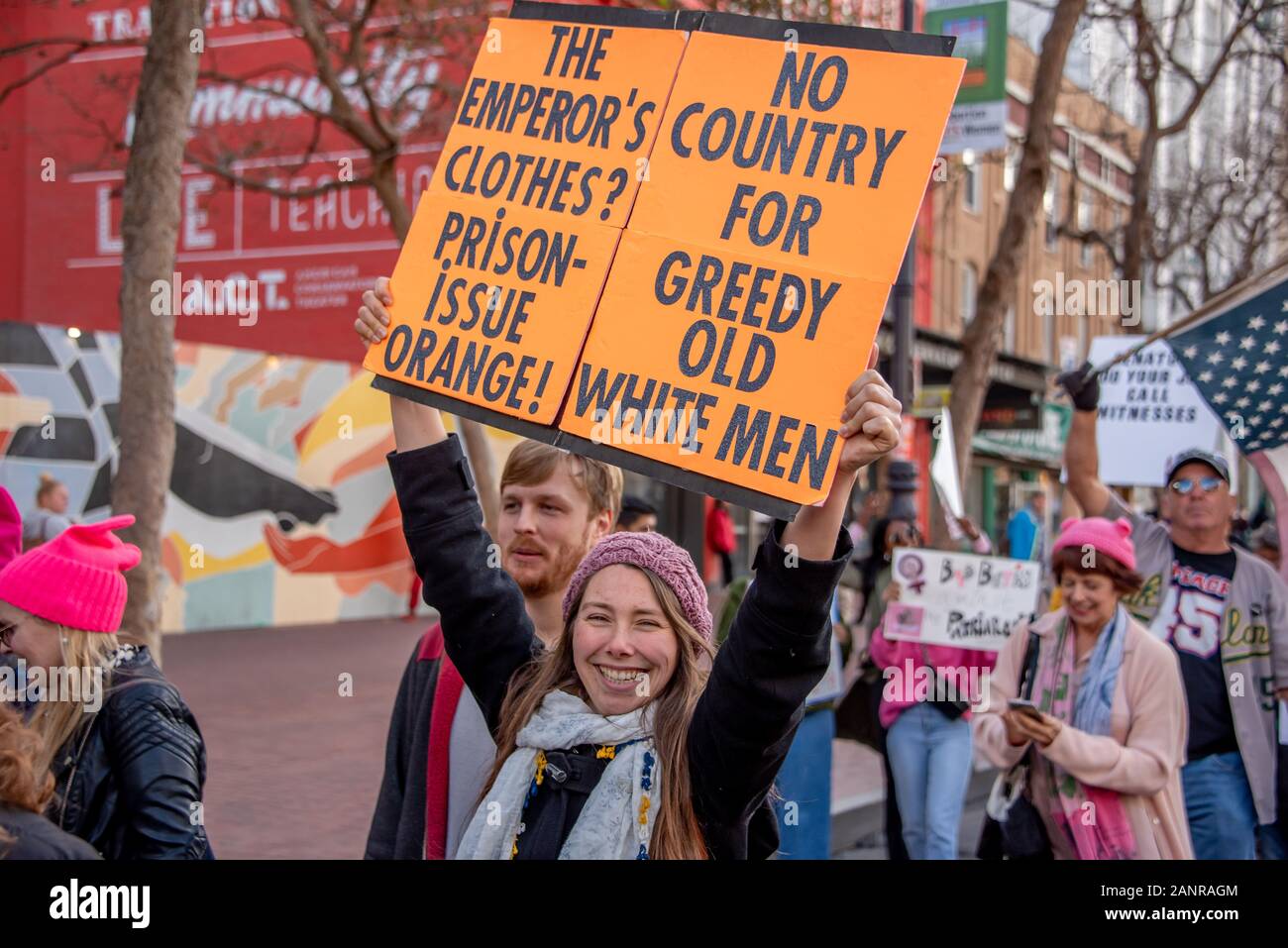 San Francisco, USA. Januar 2020. Der 4. Jährliche Frauenmarsch in San Francisco, Kalifornien. Eine Frau lächelt, während sie ein Schild hoch liest "Die Kleidung des Kaiser? Gefängnis-Ausgabe Orange!" und "kein Land für gierige alte weiße Männer." Stockfoto