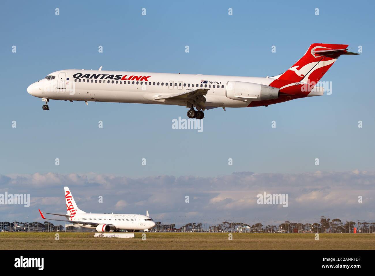 Boeing 717 regionale Airliner betrieben von QantasLink Ansatz am Flughafen von Melbourne mit einer Jungfrau Boeing 737 Rollen im Hintergrund zu landen. Stockfoto