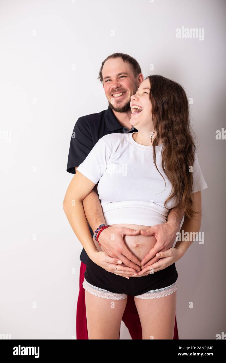 Zugeschnittenes Bild der schönen schwangeren Frau und ihrem stattlichen Mann umarmen den Bauch Stockfoto