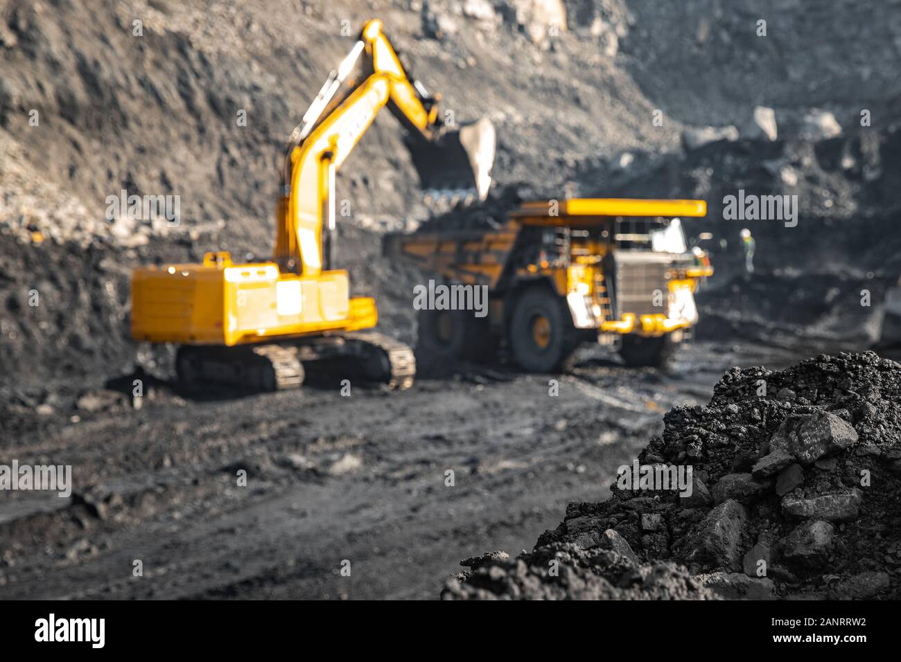 Fokus auf harte schwarze Kohle, industrielle Steinbruch geöffnet. In Hintergrund verschwommen Laden von Mineralien anthrazit Bagger in großen gelben Lkw Stockfoto