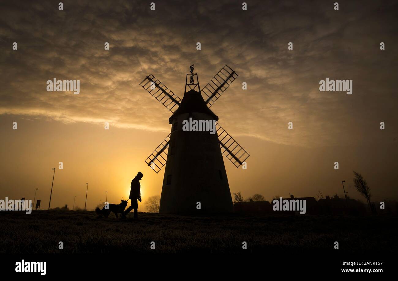 Ein Mann nimmt seinen Hund für einen Spaziergang, als die Sonne hinter dem Allen Clarke Memorial Windmühle in Blackpool steigt, wie die kalten Wochenende mit dem Quecksilber Eintauchen unter Null und Beschichtung große Teile des Landes fortgesetzt. Stockfoto