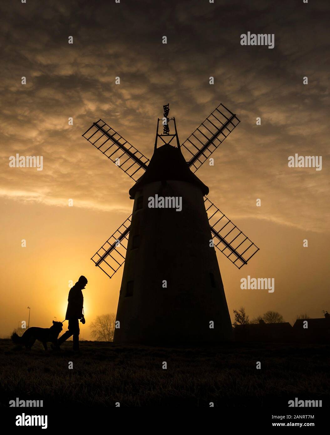 Ein Mann nimmt seinen Hund für einen Spaziergang, als die Sonne hinter dem Allen Clarke Memorial Windmühle in Blackpool steigt, wie die kalten Wochenende mit dem Quecksilber Eintauchen unter Null und Beschichtung große Teile des Landes fortgesetzt. Stockfoto