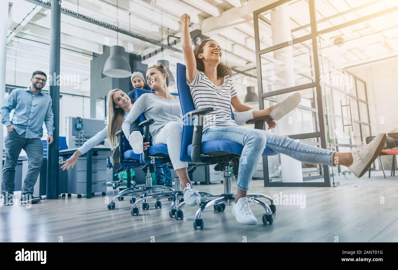 Junge freundliche Geschäft Leute in ungezwungener Kleidung Spaß am Rudern Stühle in einem modernen Büro. Happy Team Konzept. Stockfoto