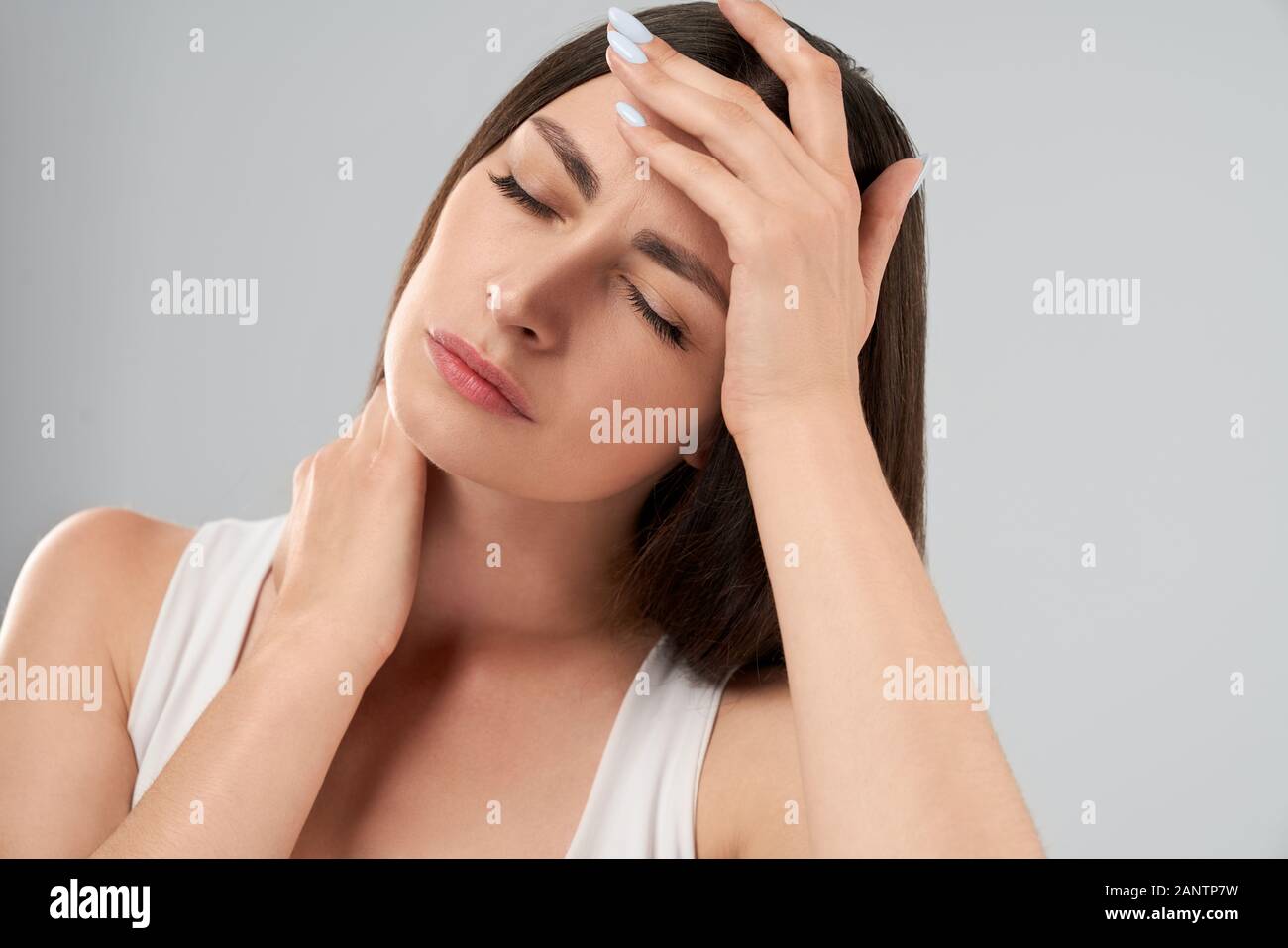 Clolse bis der hübschen weißen Frau in weißem Hemd Posing über Grau isoliert Hintergrund und berühren mit der Hand, weil der Migräne. Crop von brunette leiden unter Schmerzen. Stockfoto