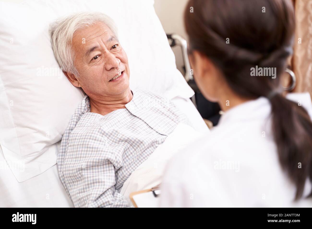 Jungen asiatischen Arzt im Gespräch mit älteren Patienten am Krankenbett in hosptial Ward Stockfoto