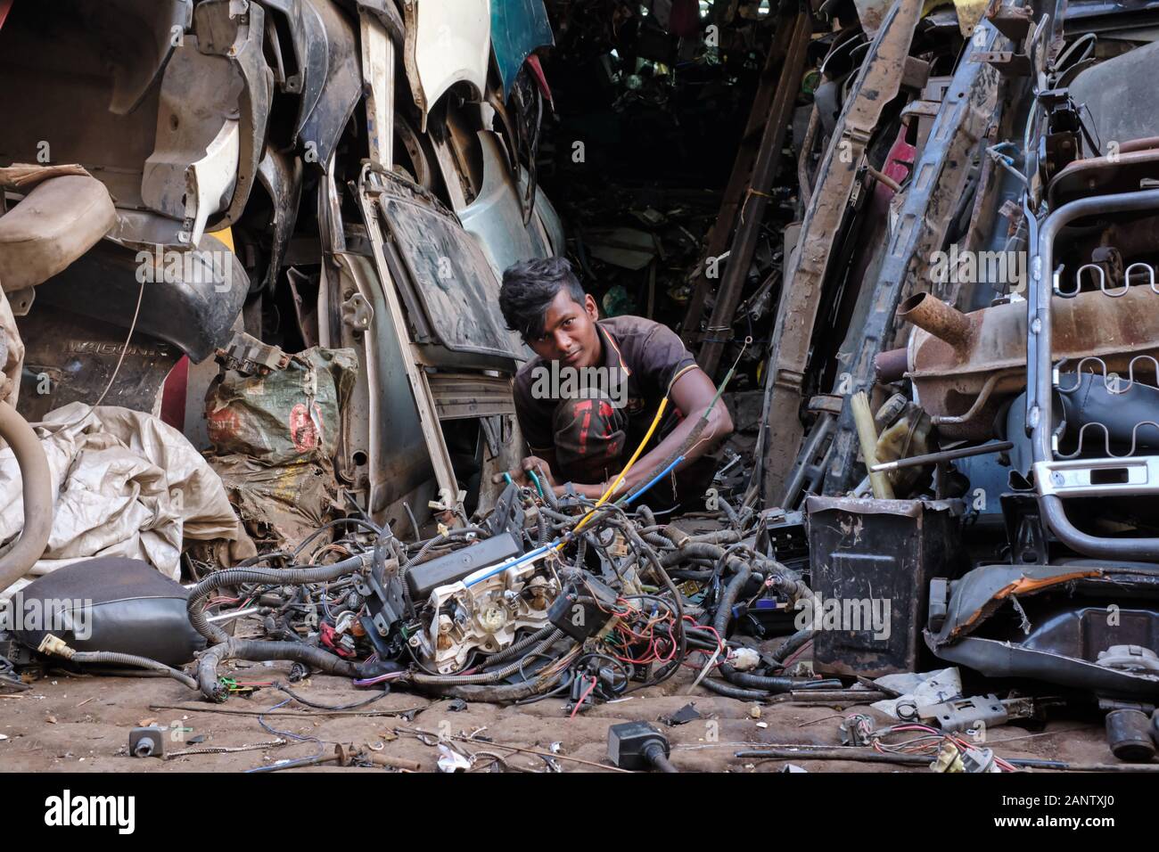Ein Arbeiter, der Teile zerlegter alter Autos auf Dem Diebemarkt (Chor Bazar) in Mumbai, Indien, von einem Berg alter Autoteile umringt, auseinandernimmt Stockfoto