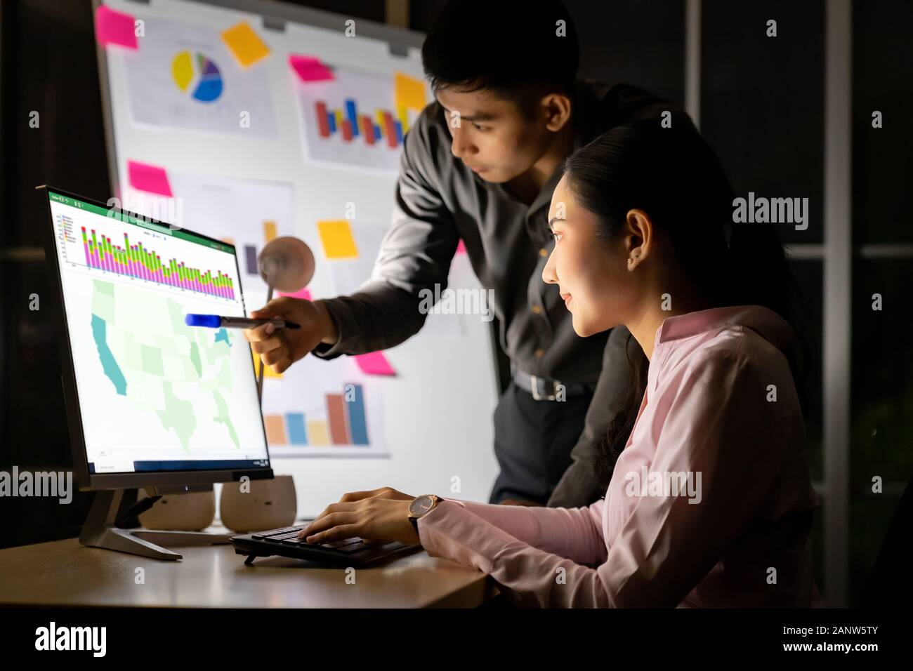 Junge Erwachsene asiatische Unternehmer diskutieren mit Kollegen über die Arbeit mit der Analyse Grafik auf dem Whiteboard spät in der Nacht in ihrem Büro mit Computer. Stockfoto