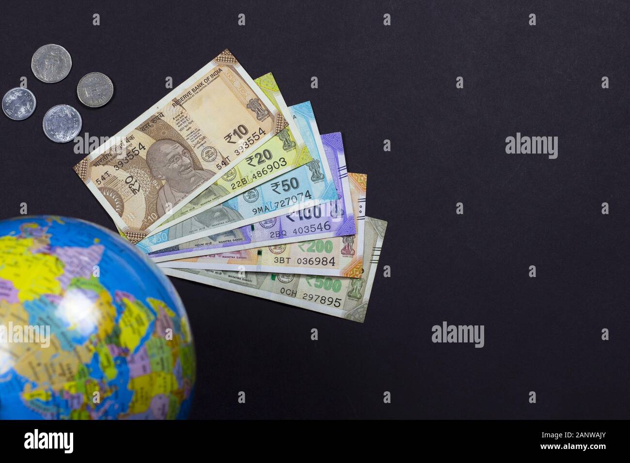 Kopf auf Schuss von indischen Banknoten von 10.20.50.100.500 Rupien und Münze oder Pfennig mit einem Weltkarten-Globus auf schwarzem Hintergrund mit Kopierraum für Text. Stockfoto