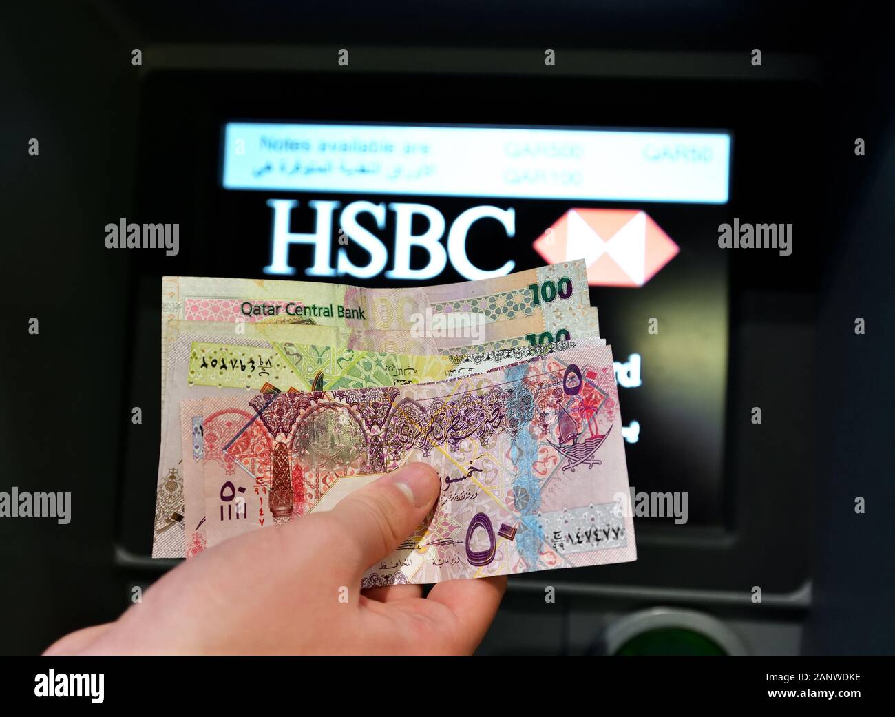 Doha, Katar - Nov 17. 2019. Katarische Riale in der Hand auf dem Hintergrund des Geldautomaten der HSBC Bank Stockfoto