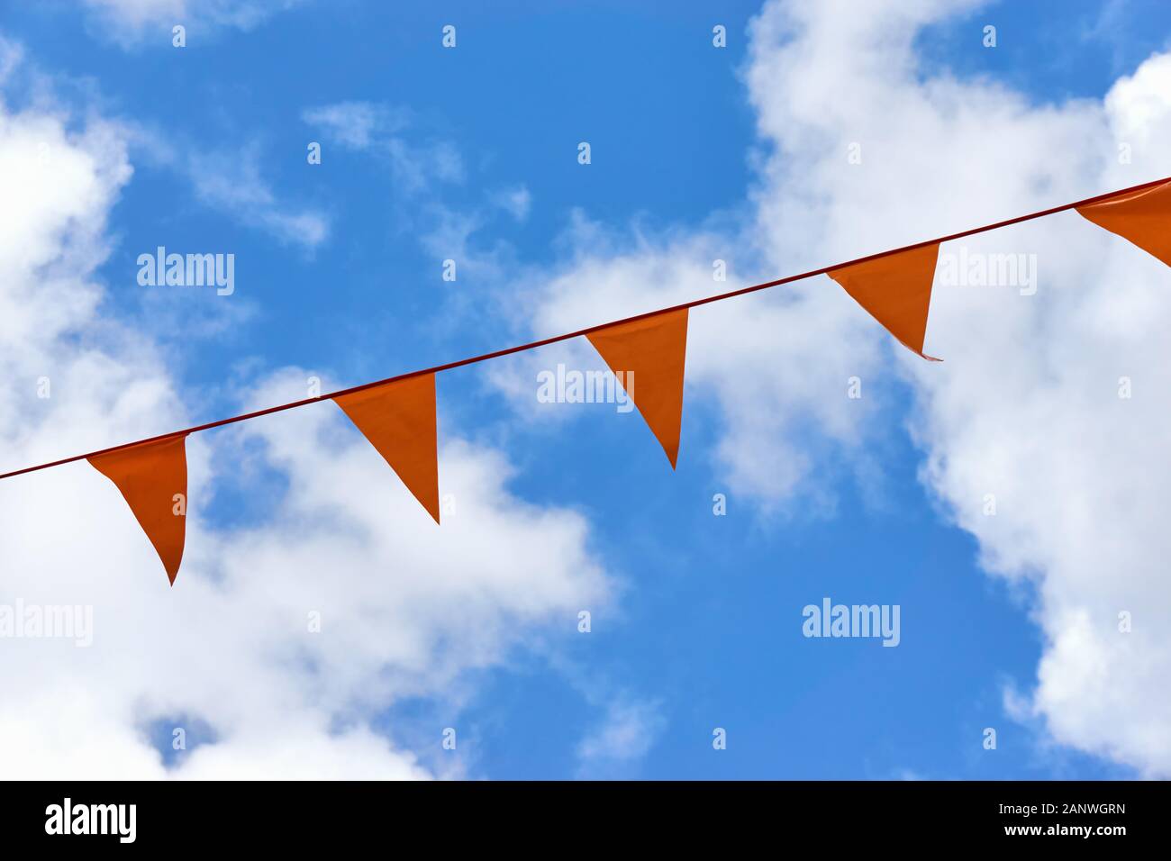 Eine Reihe orangefarbener Dreiecksfahnen auf Koningsdag. Ein nationaler Urlaub in den Niederlanden gegen einen blauen Himmel mit Wolken und Kopieraum Stockfoto