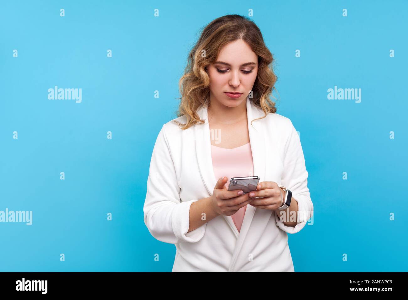 Portrait von ernsthaften Geschäftsfrau mit gewelltes Haar in weisse Jacke eingeben Nachricht mit Handy mit konzentriertem Blick fokussiert, ad mobiler Apps, auf Stockfoto
