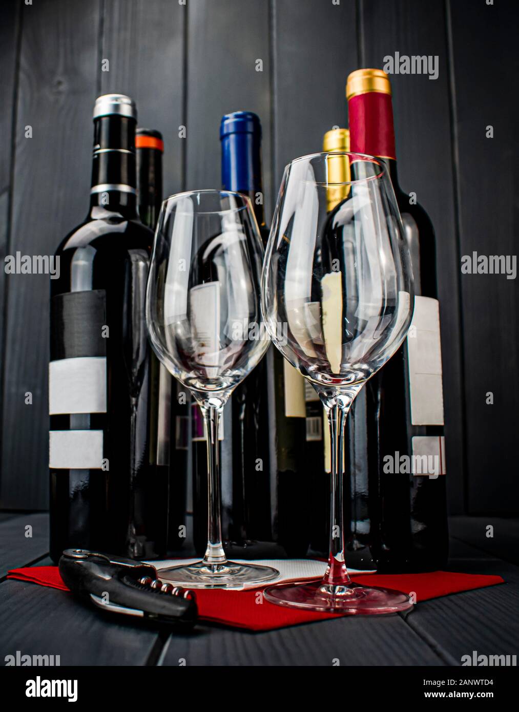 Glänzend Glas Tassen auf tief rot Tischdecke, Korkenzieher und vier Flaschen Rotwein liegen und ruht auf sich Entkorkt zu werden und schmeckte Stockfoto