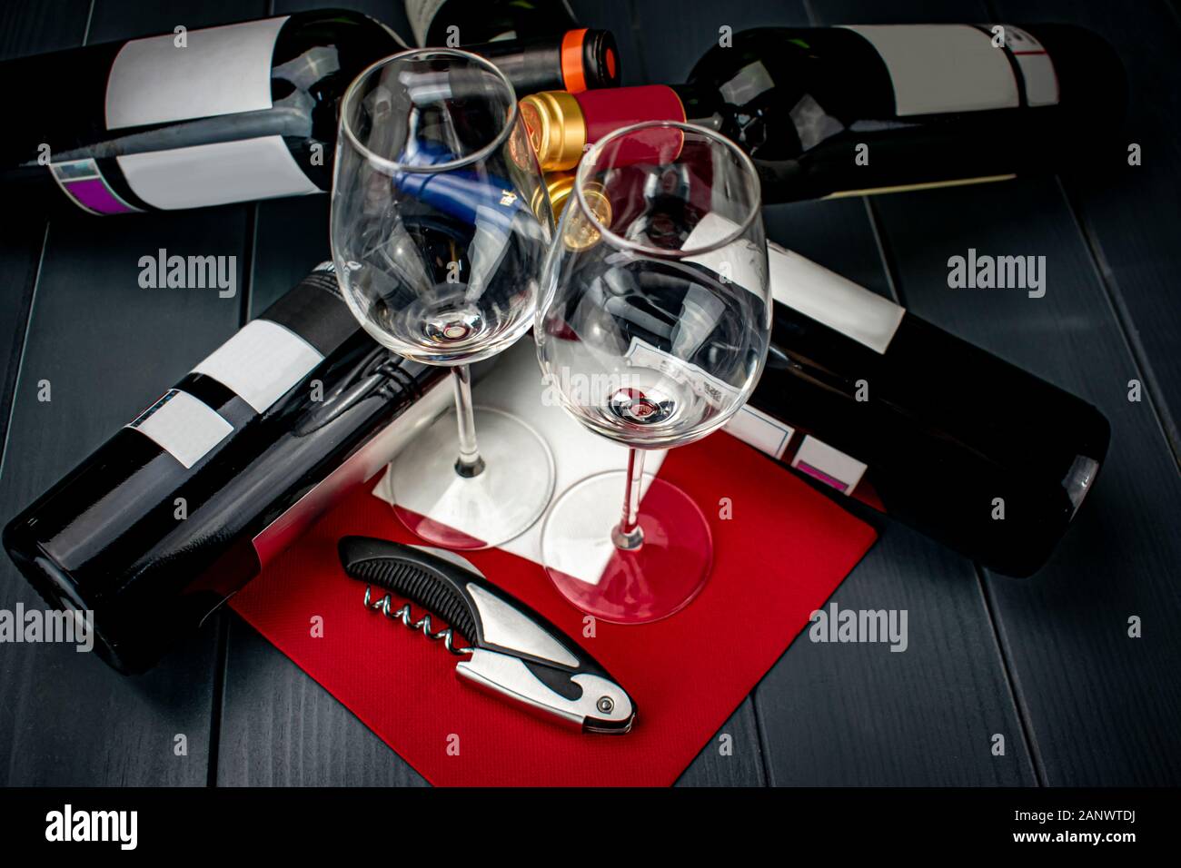 Glänzend Glas Tassen auf tief rot Tischdecke, Korkenzieher und vier Flaschen Rotwein liegen und ruht auf sich Entkorkt zu werden und schmeckte Stockfoto