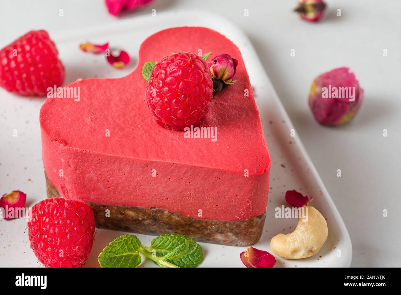 Raw vegan Himbeere herzförmige Kuchen oder Käsekuchen mit frischen Beeren, Nüsse, Minze und getrockneten Blumen. Valentines Tag Dessert. Nach oben Schließen Stockfoto