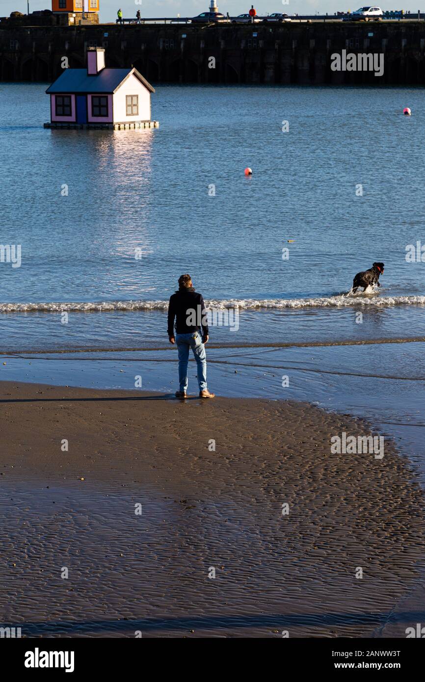 Folkestone, Kent. GROSSBRITANNIEN. Ein versunkenes Haus im Hafen. Ein Mann schaut auf seinen Hund, der im Hafen paddelt. Stockfoto