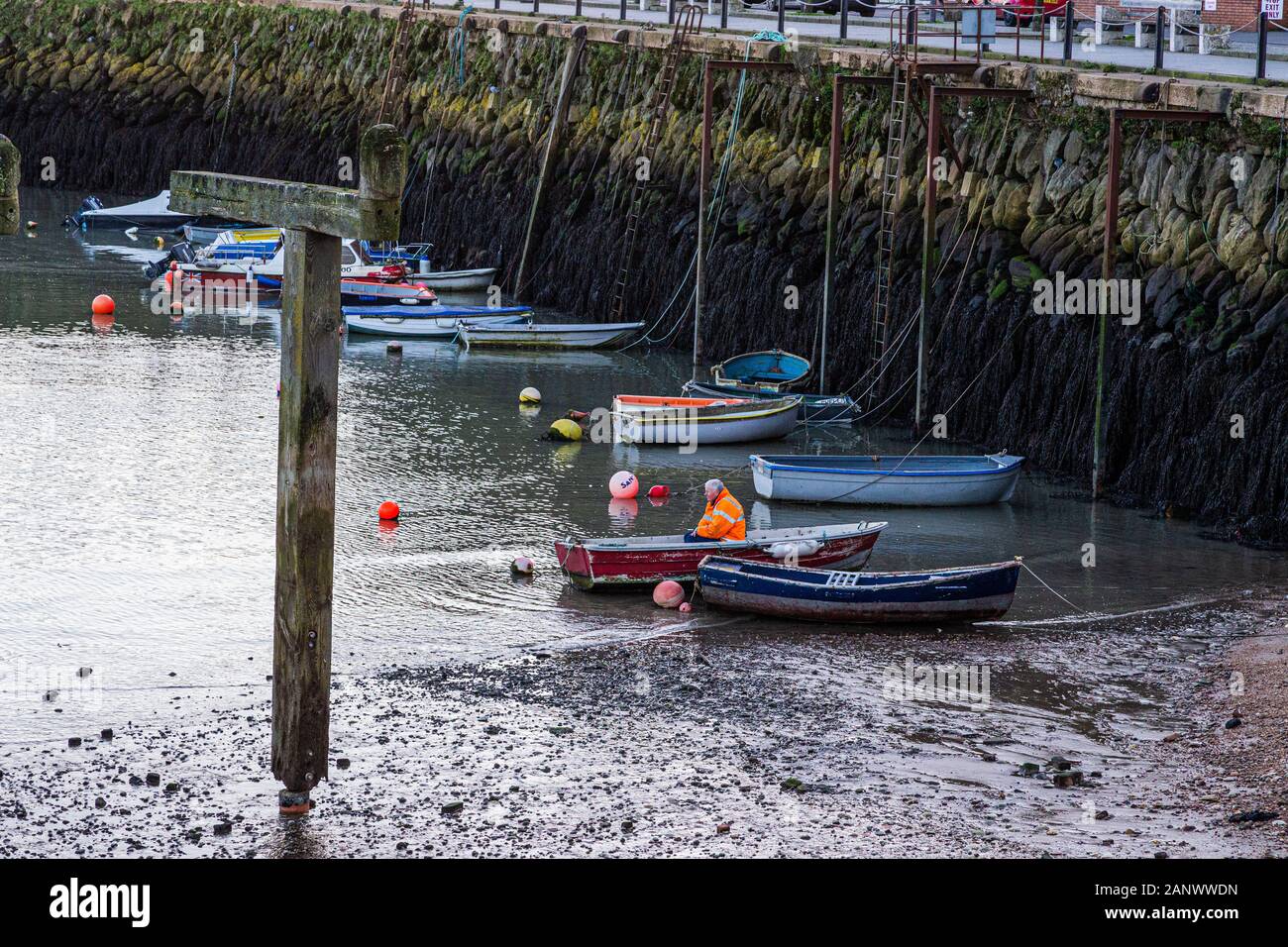 Folkestone, Kent. GROSSBRITANNIEN. Verschiedene Farben von Ruderbooten, die im Hafen von Folkestone gegen mit Algen bedeckte Felsen gefesselt sind. Stockfoto