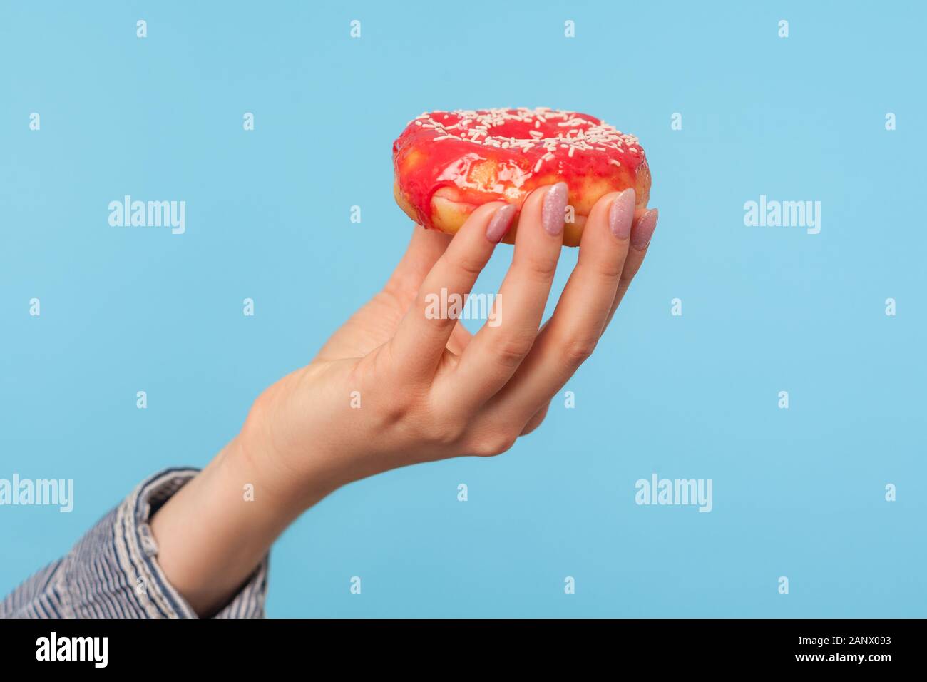 Nahaufnahme der weiblichen Hand mit köstlichen glasierten rot Donut mit Streuseln, leckere Krapfen, süß Süßwaren hoch in Glukose und Kalorien. Stockfoto