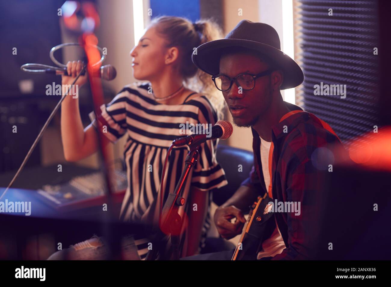 Porträt des zeitgenössischen afroamerikanischen Mann spielt Gitarre und Gesang auf das Mikrofon während der Probe oder ein Konzert mit Musik Band in schwach Studio lit Stockfoto