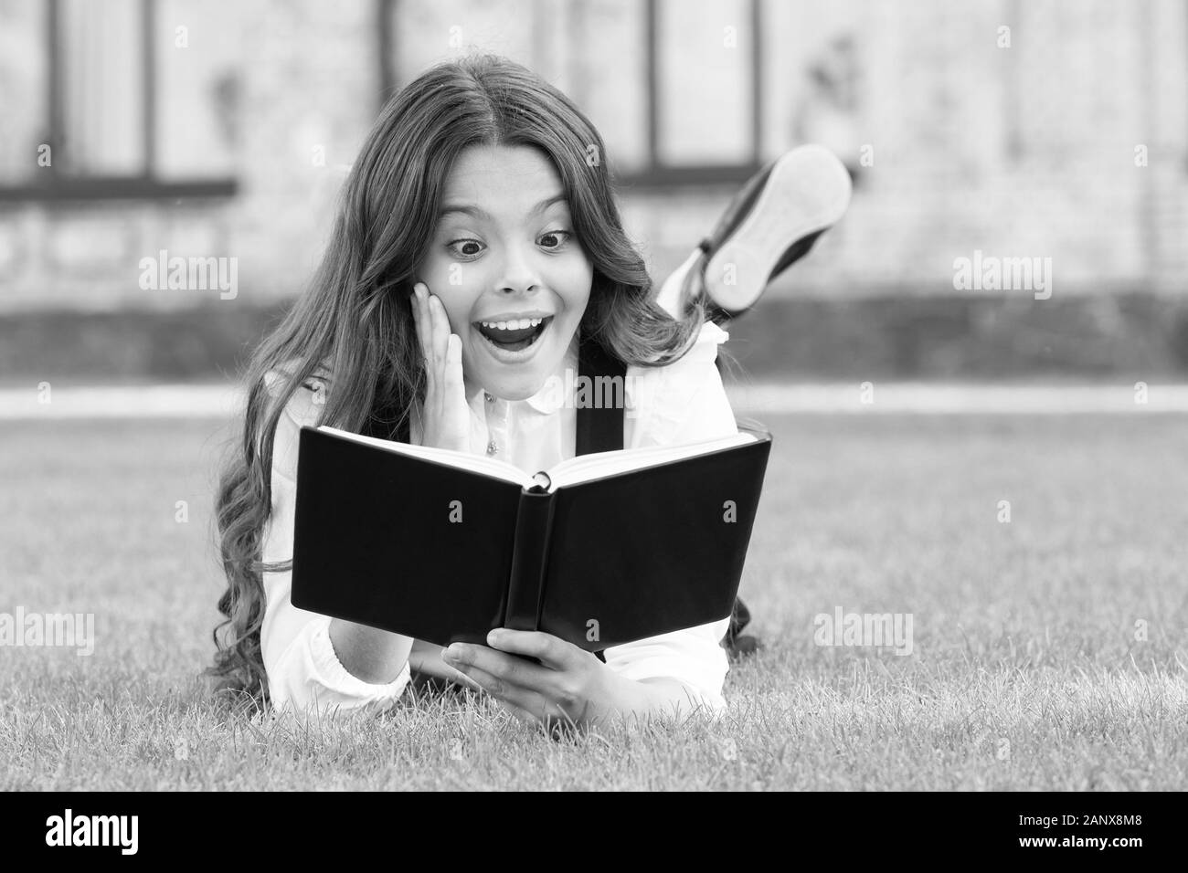 Buch mit unerwartete Überraschung. Überrascht kind Buch lesen auf grünem Gras. Kleines Mädchen Lesung mit Überraschung Emotion auf das Gesicht. Süße kleine Schulmädchen halten Mund große Überraschung geöffnet. Lassen Sie sich überraschen. Stockfoto