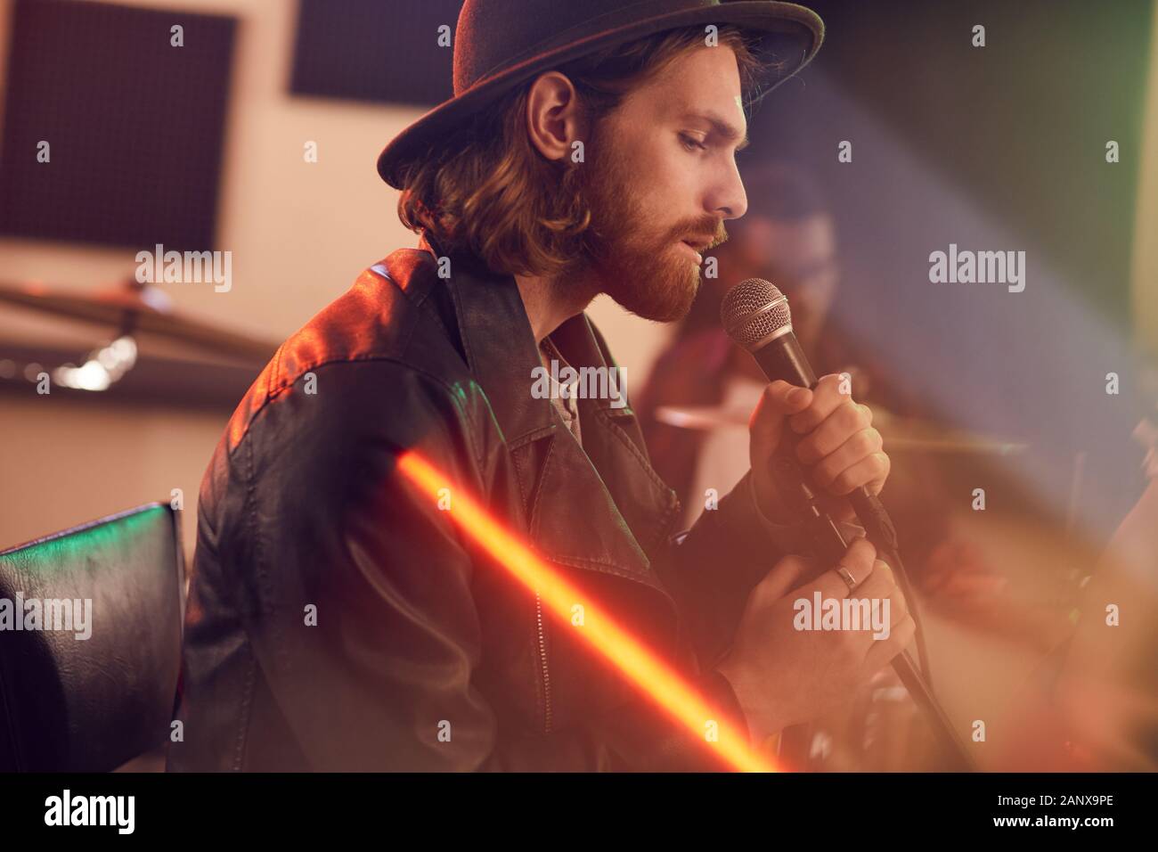 Seitenansicht Portrait von Stattlichen bärtiger Mann singen auf das Mikrofon während der Musik Konzert mit zeitgenössischer Band im Studio, Kopie Raum Stockfoto