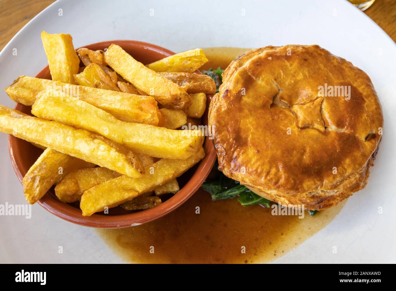 Typische deftig, lecker British Pub grub Mahlzeit: warmes Fleisch Torte in Soße mit einer Schüssel mit Golden gebratene chunky Chips auf ein weißes Porzellan Teller serviert Stockfoto