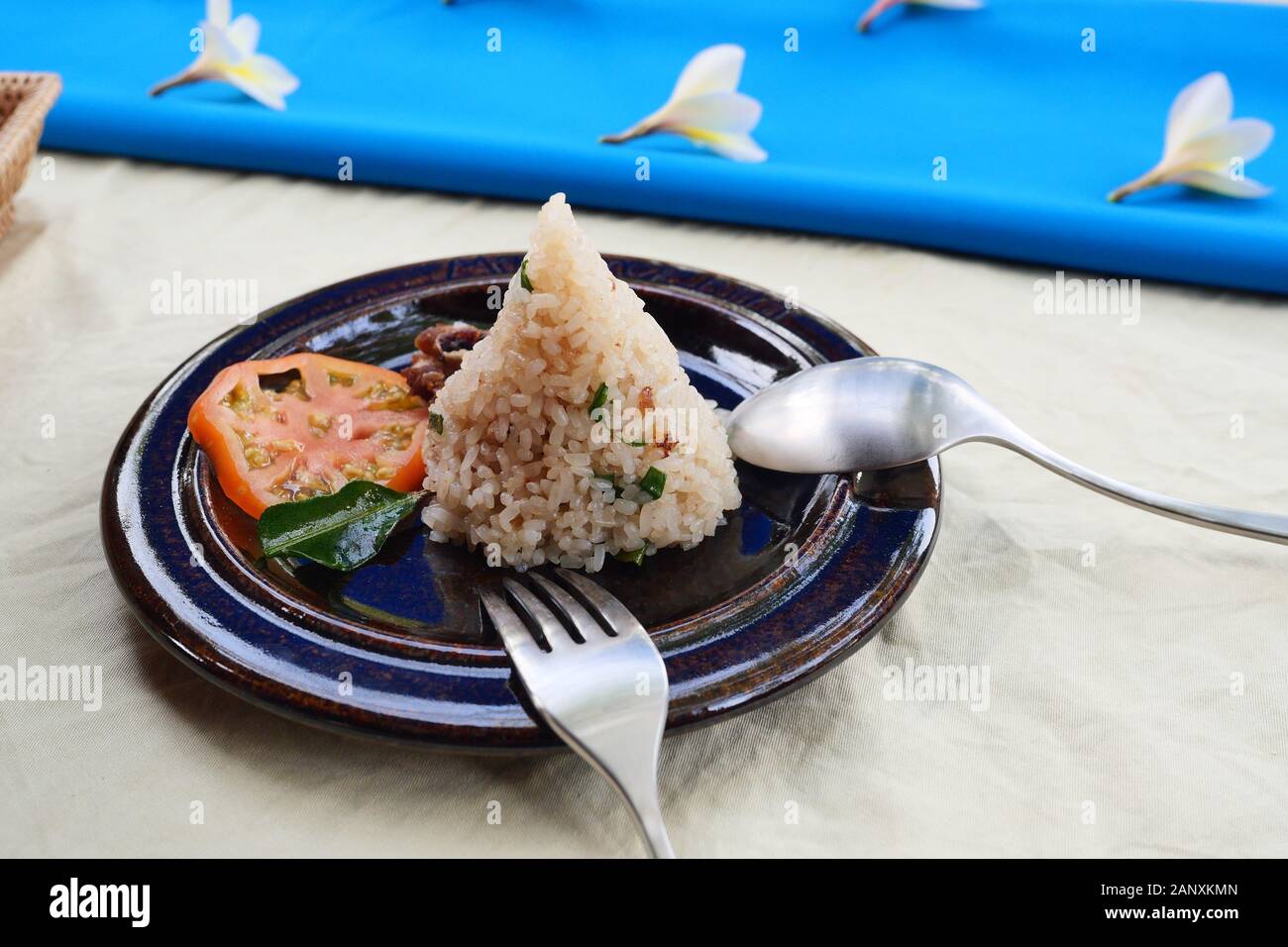 Zongzi oder traditionelles Chinesisch klebrigen Reis Knödel mit in Scheiben geschnittenen Tomaten mit Löffel und Gabel auf Teller, chinesisches Essen am Tisch in Weiß und Blau abgedeckt Stockfoto