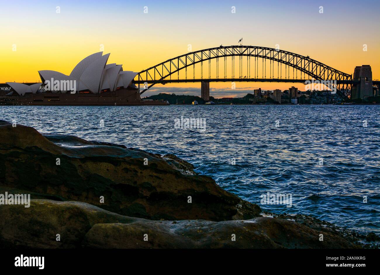 Sydney, AUSTRALIEN - 10. MÄRZ 2018 - Sydney Opera House und Harbour Bridge, die Wahrzeichen der Stadt, von der natürlichen Küstenlinie bei Sonnenuntergang aus gesehen Stockfoto