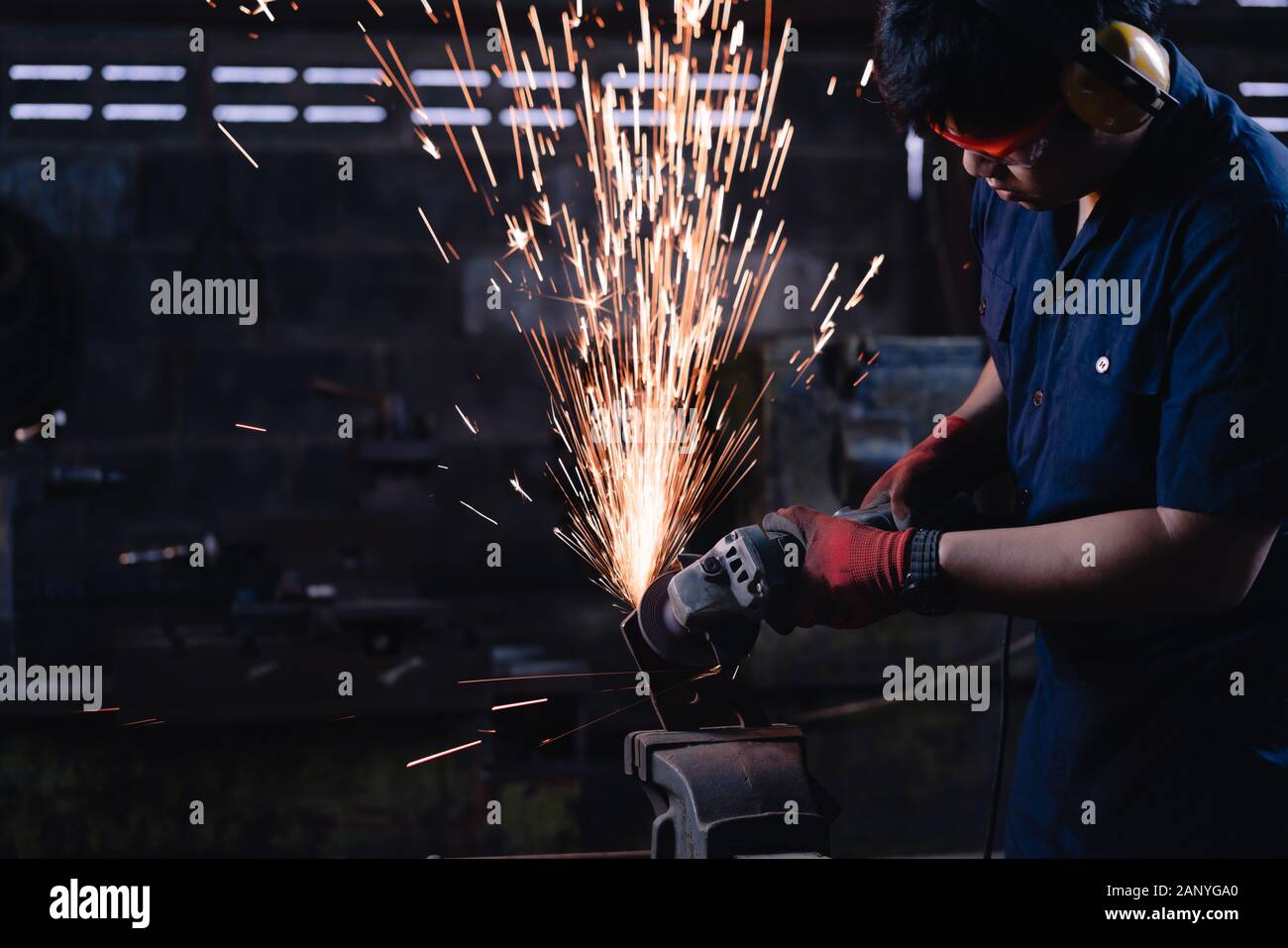 Industrielle Metallarbeiter in Asien tragen Schutzkleidung und verwenden in dunklen Produktionsbetrieben Stromwerkzeuge und -Geräte mit hellen heißen Funken und Kopierräumen Stockfoto