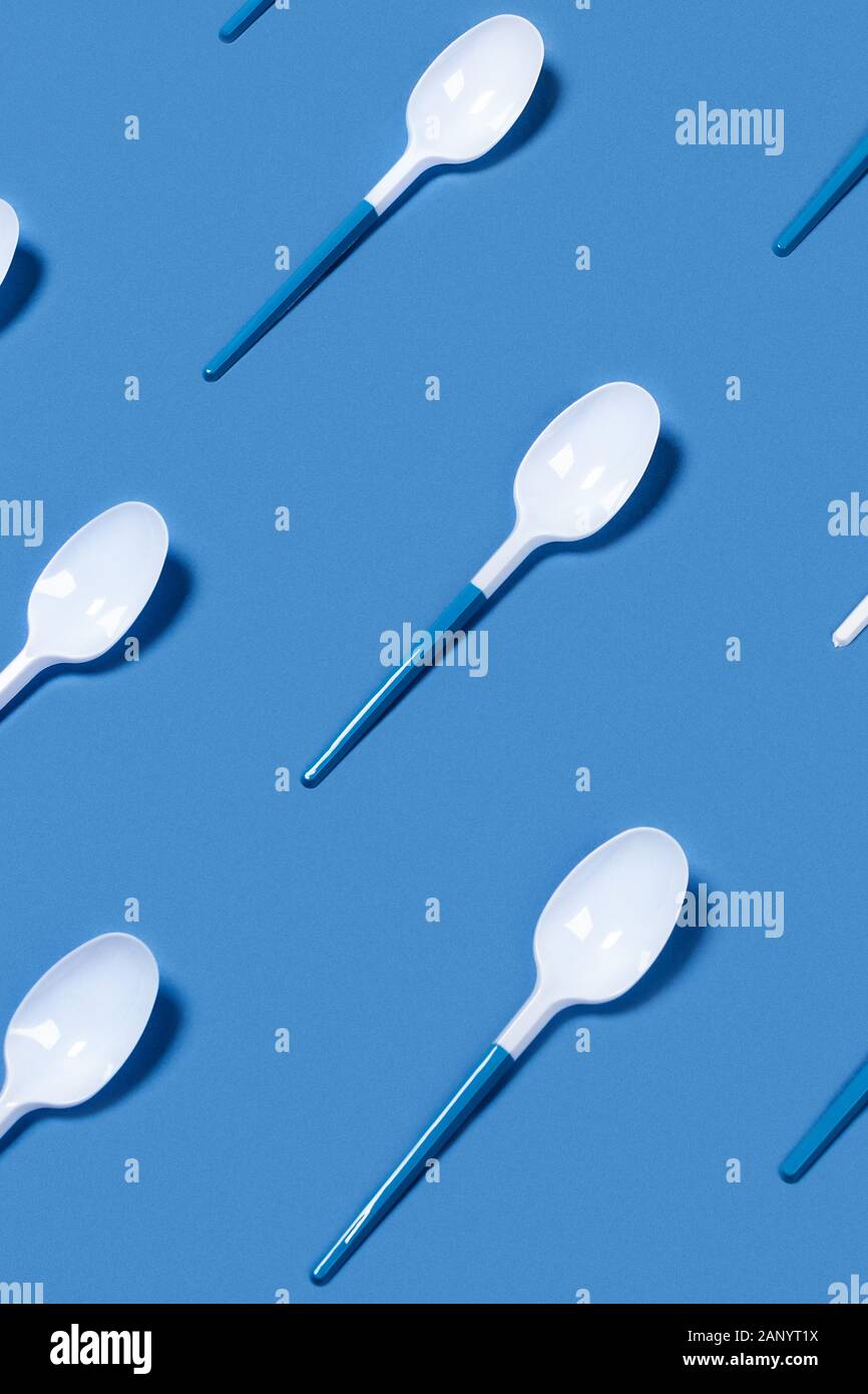 Muster aus weißem Kunststoff Löffel auf blauem Hintergrund. Vertikale Bild. Flach, Ansicht von oben. Stockfoto