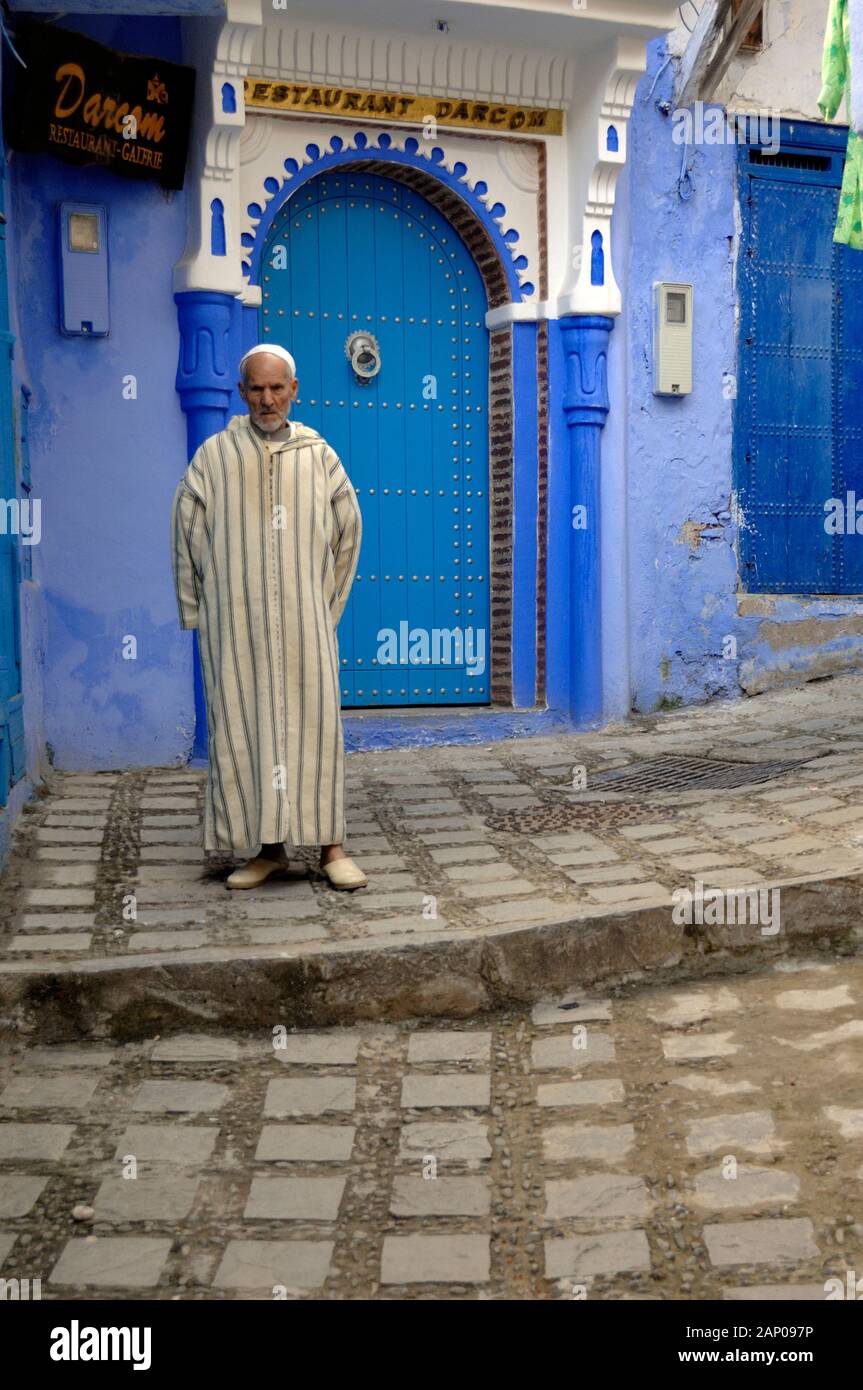 Marokkanischen arabischen Mann, Kammgarn Djellaba vor der blauen Tür des Restaurants in der Medina oder die alte Stadt Chefchaouen oder Chaouen Marokko Stockfoto