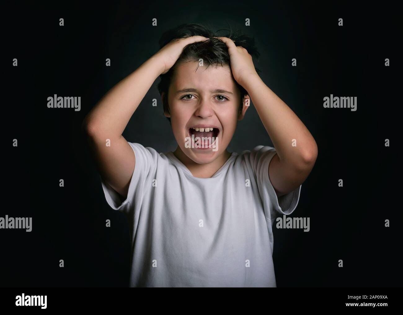 Wütend und betonte Kind mit seiner Hände auf seinen Kopf auf schwarzem Hintergrund Stockfoto
