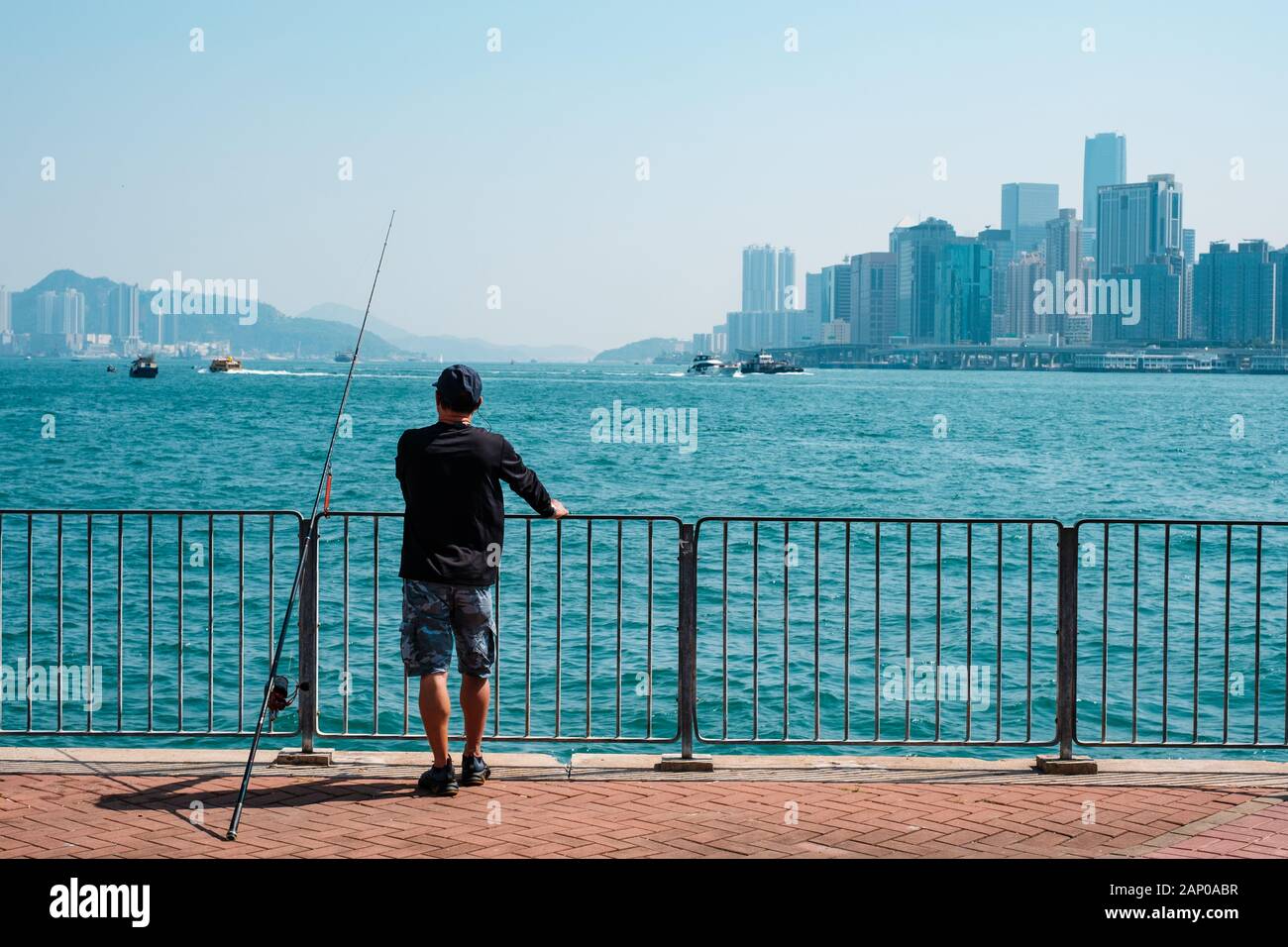 Fisher Mann mit angelrute an der Küste mit Skyline von Hong Kong, Kowloon Stockfoto
