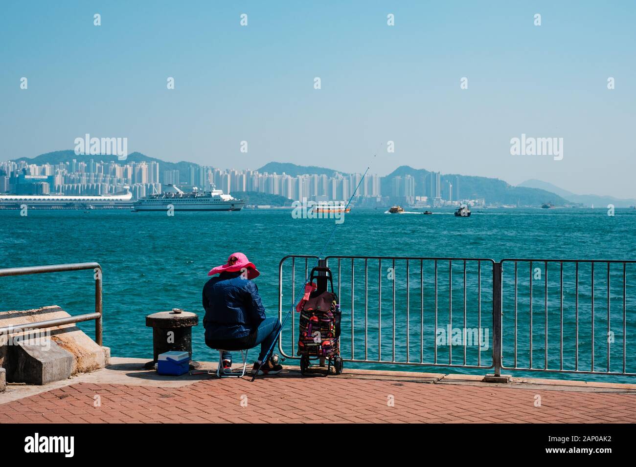HongKong, China - November, 2019: Fisher Mann oder Frau mit Angelrute sitzen auf Küste mit HongKong Skyline im Hintergrund Stockfoto