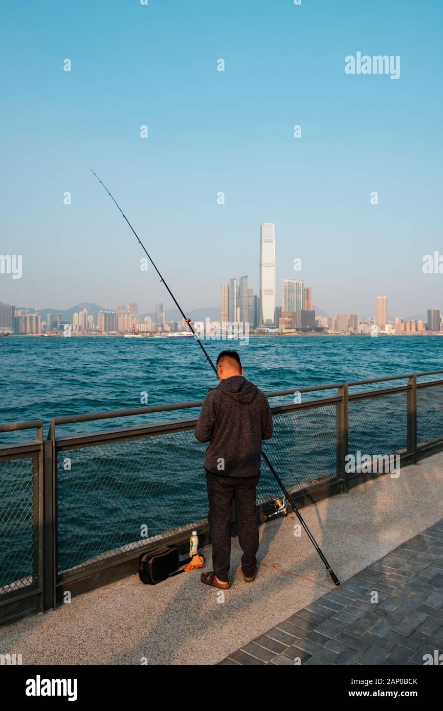 Fisher Mann mit angelrute an der Küste mit Skyline von Hong Kong, Kowloon Stockfoto