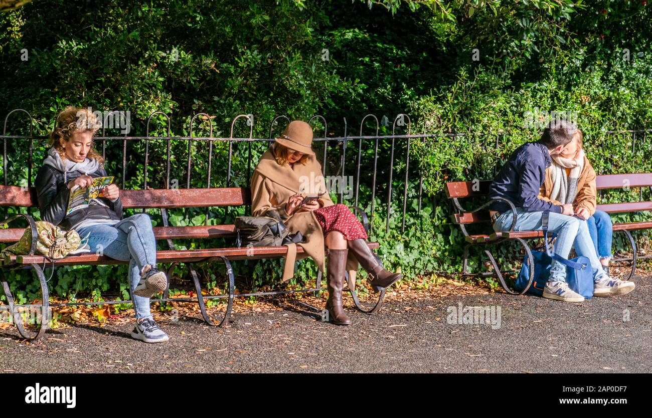 Frauen lesen und Paar küssen Auf Parkbank in Dublin in Irland. Stockfoto