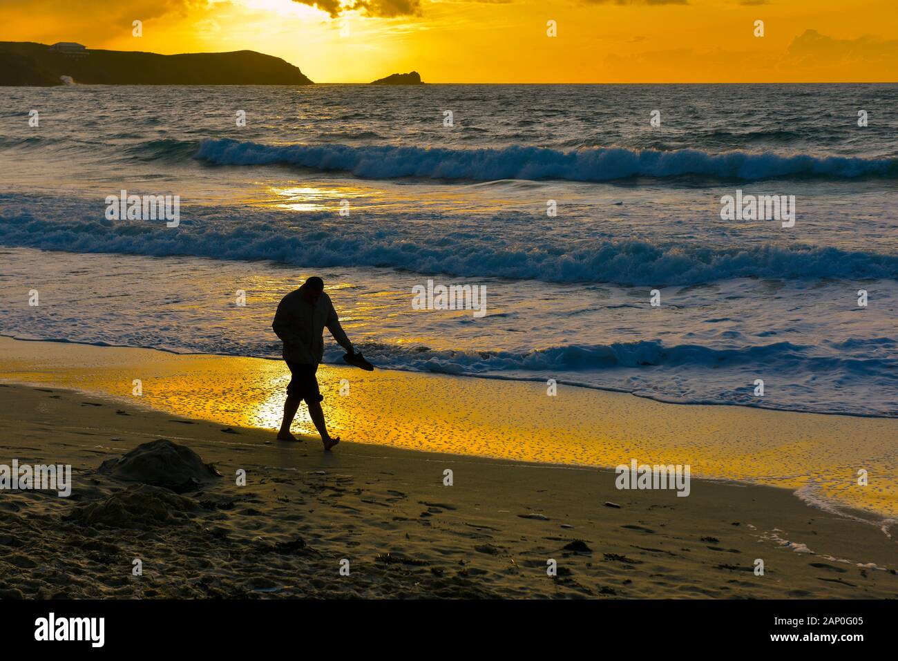 Ein Mann zu Fuß entlang der Küste durch eine schöne intensive Sonnenuntergang am Fistral in Newquay in Cornwall. Stockfoto