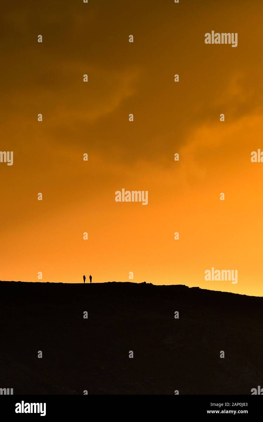 Die winzigen Figuren von zwei Wanderer Silhouette gegen einen intensiven Sonnenuntergang in Newquay in Cornwall. Stockfoto