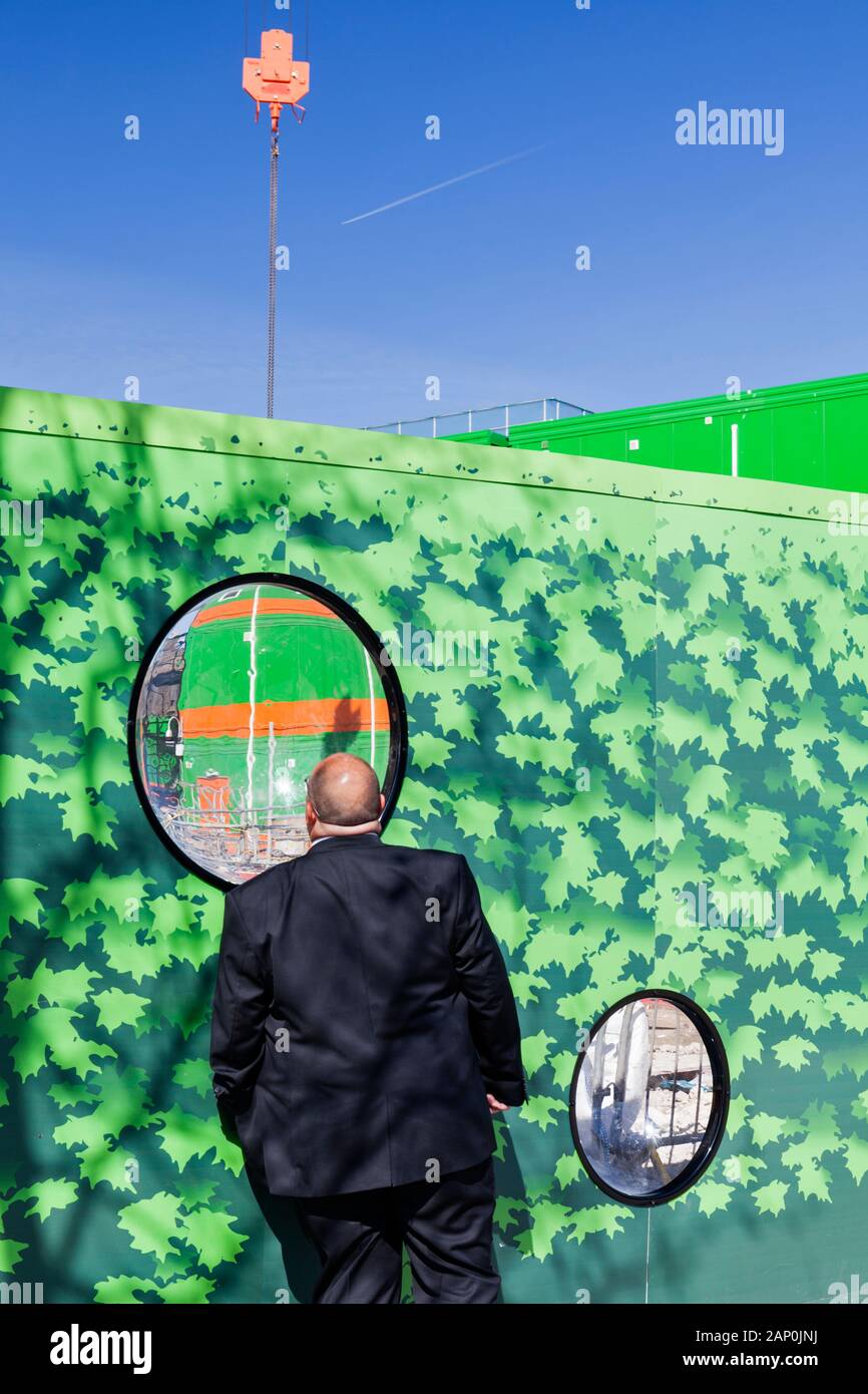 Einen geeigneten Mann views laufenden Bauarbeiten durch große runde Fenster auf architektonische Werbetafeln. Stockfoto