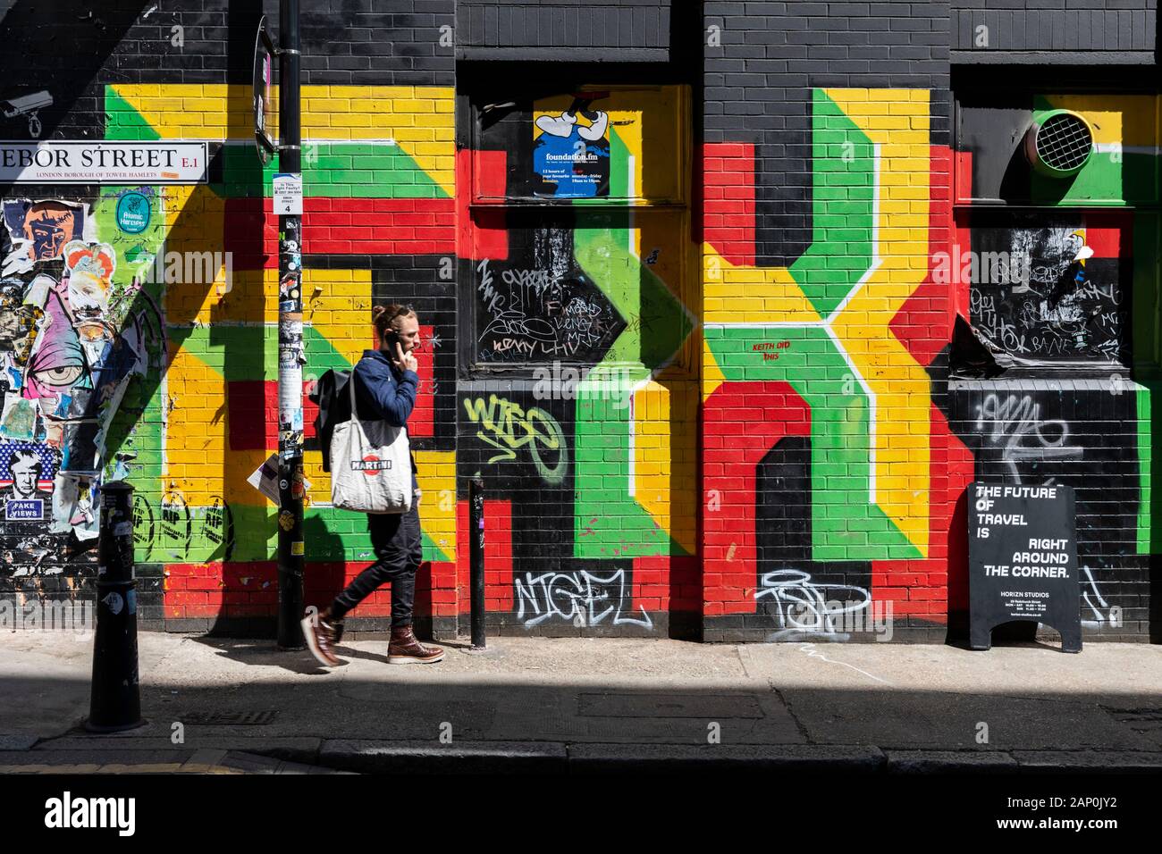 Ein junger Mann auf einem Mobiltelefon Wanderungen vorbei an bunten Wand Graffiti auf Ebor Street in Shoreditch. Stockfoto