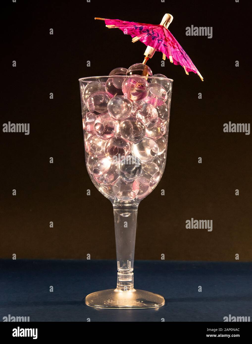 Ein Weinglas aus Kunststoff, das mit Wasserperlen gefüllt ist, um einen Cocktail zu machen - mehr für Blumen als für Menschen. Stockfoto